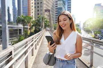 Portrait of smiling girl on footbridge watching her smartphone in the modern sustainable metropolis of Sao Paulo, Brazil