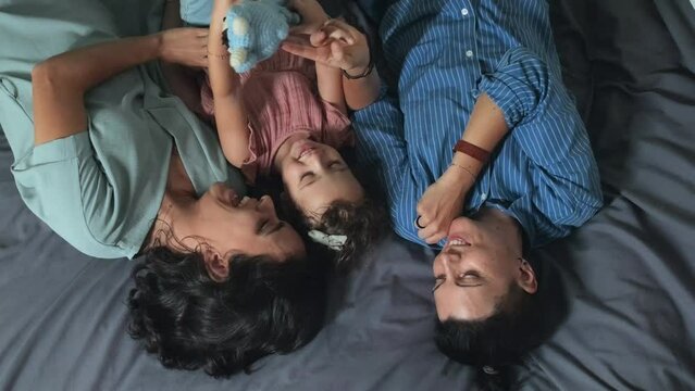 Top view of romantic same-sex female couple and their 2 year old daughter lying together on bed at home during leisure time
