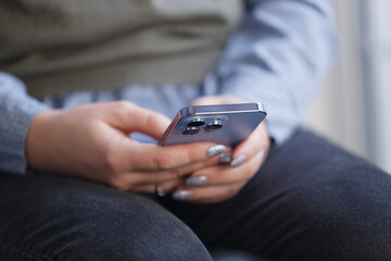 Young woman holding smart phone and browsing app. Close up photo of modern blue mobile phone in female hands