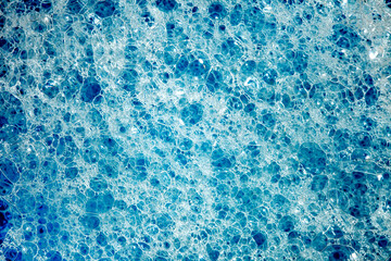 Foam on surface of liquid blue detergent, bubbles different size, close-up full depth of field, top view