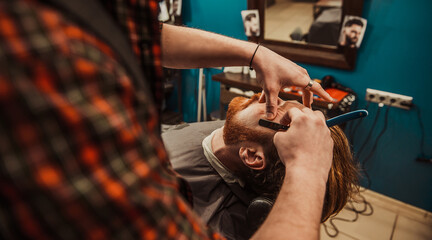 Fototapeta na wymiar A professional barber cuts his beard to a young hipster man.
