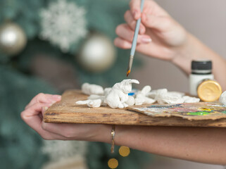 .a young woman makes Christmas toys out of clay and paints them with paints. hand and palette close-up