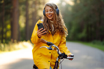 Fototapeta na wymiar Pretty young womanusing mobile phone in the city while listening music through earphones to go by the bicycle in the park. Lifestyle. Relax, nature concept.