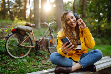 Pretty young womanusing mobile phone in the city while listening music through earphones to go by the bicycle in the park. Lifestyle. Relax, nature concept.