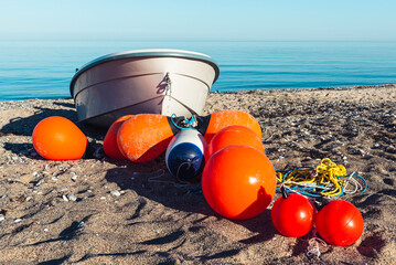 Orange Bojen und ein Fischerboot liegen auf einem Sandstrand am Ufer der Ostsee in der Sonne,...