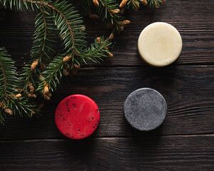 Three pieces of handmade soap on dark wooden background with green pine tree. 