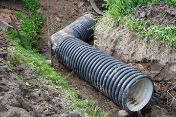 black wide pipe lies at an angle in the ditch in the summer