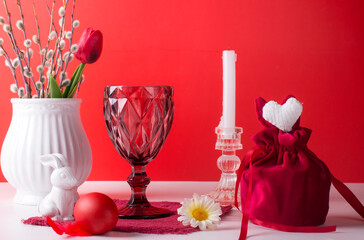 Easter still life with a white rabbit on a red background. A glass of wine and painted eggs - the concept of a bright Easter holiday