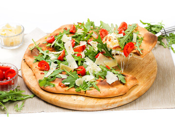 Pizza on a wooden top from which a slice is cut. Isolated photo on a white background. Ingredients: tomatoes, parmesan cheese, arugula. Traditional Italian pizza concept side view.