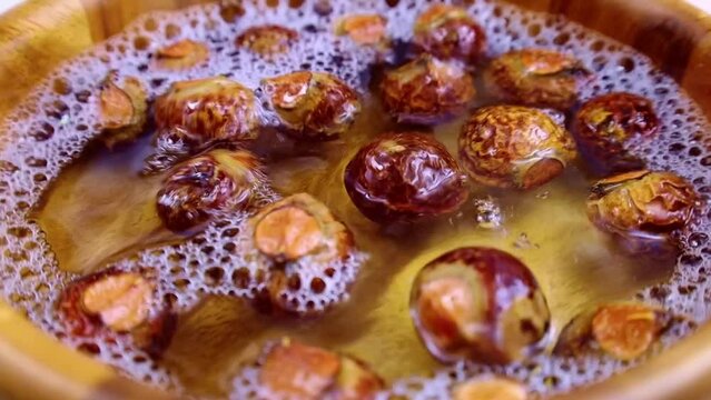 Brown dry soap nuts (Soapberries, Sapindus Mukorossi, Reetha) for organic laundry and gentle natural skin care falling in the water with circle rotation close up