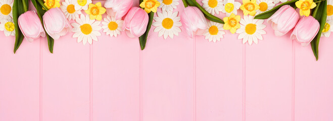 Top border of springtime flower decorations. Overhead view on a pastel pink wood banner background. Copy space.