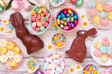 Easter candy table scene. Overhead view over a white wood background. Chocolate bunnies, candy eggs and a variety of sweets. - Powered by Adobe