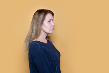 Sad middle-aged woman looking away on orange background, woman 45 years old, hair is starting to turn gray, woman does not want to grow old, wants to be always young and fresh