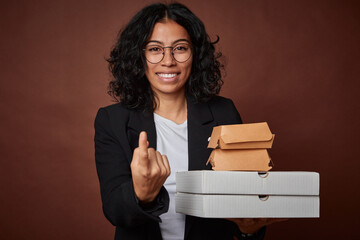 Naklejka premium Young business woman holding a fast food pack pointing with finger at you as if inviting come closer.
