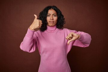 Young colombian curly hair woman isolated on brown background showing thumbs up and thumbs down,...