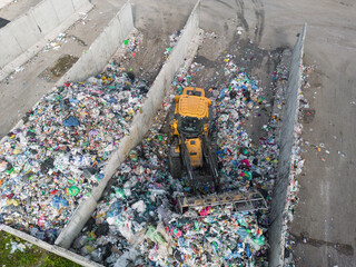 Skid steer loader moving plastic garbage with scrap grapple on the landfill site, drone shot. Waste disposal concept.