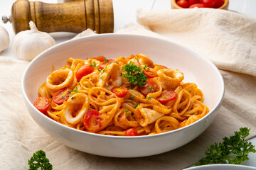 Linguine pasta with squid and cherry tomato in tomato sauce in white plate