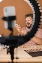Famous blogger. Cheerful male vlogger showing cosmetics products while recording video and giving advices for his beauty blog. Make-up artist and recording beauty vlog concept