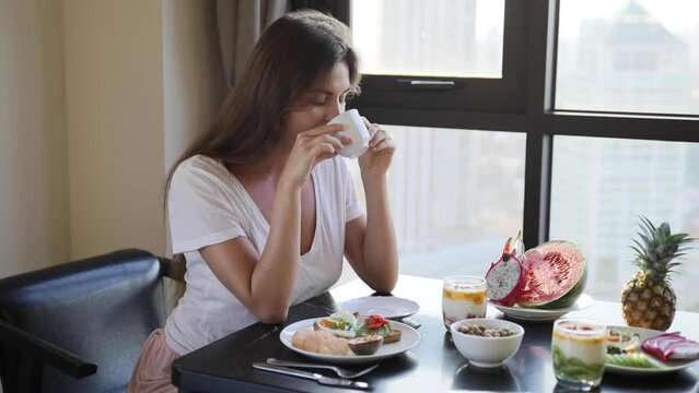 Young woman drinking coffee or tea during breakfast
