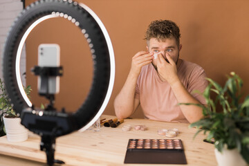 Male beauty blogger with makeup product recording video at home. Using ring lamp and smartphone. Vlog cosmetic products and diversity concept