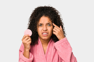 Young african american woman wearing a pink bathrobe holding a cellulose disk showing a disappointment gesture with forefinger.