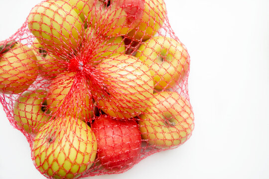 Apples in a red net. ECO Shopping - apples in the net. Convenient purchases in the store - packaged apples in a sebka. Apples are yellow with red in one grid on a white table.