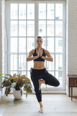 short haired woman standing in yoga tree pose in home loft interior