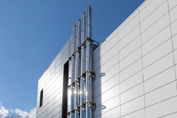 Stainless steel chimneys. Gas heating turbo boiler. Chrome ventilation pipes on the outer wall of industrial building against blue sky background. bottom-up view. Part of the building heating system
