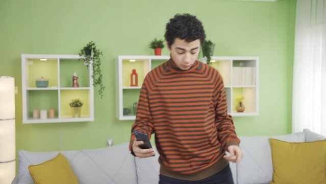 Lively positive boy dancing at home, listening to music, making social media posts.
Handsome and sympathetic boy is listening to music and dancing by making a video with his smart phone at home.
