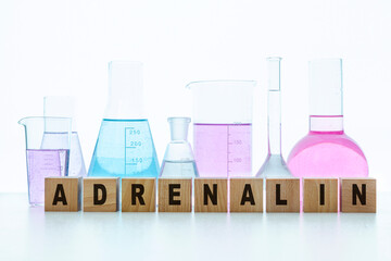 The word adrenaline is written on the cubes. In the background are flasks with multi-colored...