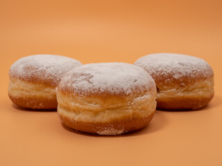 Freshly baked and dusted with powdered sugar German donuts. Donut berliner or krapfen on orange background.
