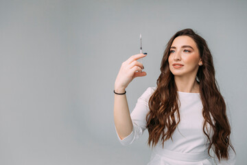 young dark-haired curly woman doctor in a white coat holds an insudin syringe for injection in her hands. Cosmetologist in a beauty salon preparing for a beauty procedure, copy space