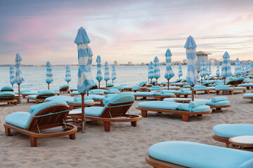 Evening beach at sunset. Empty blue wooden sunbeds and umbrellas on a sandy beach near the sea