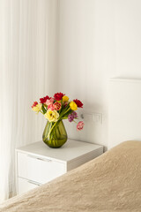 Colorful tulips on the bedside table. Fresh design. Fresh flowers in vase near bed, bedroom interior design details, cozy hotel room, apartment after renovation, modern flat with decor.