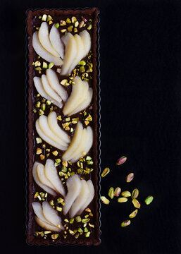 Tarta de chocolate, pera y pistachos sobre fondo negro, vista superior. Tarta fina alargada. 