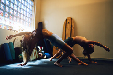 couple young woman and a man doing hatha yoga wild thing pose indoors