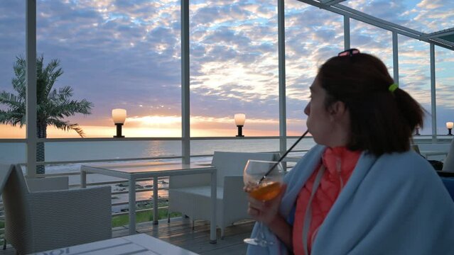 Woman drinking orange cocktail in restaurant terrace near the sea. 4k footage UHD 3840x2160 