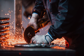 Locksmith in special clothes and goggles works in production. Metal processing with angle grinder. Sparks in metalworking.