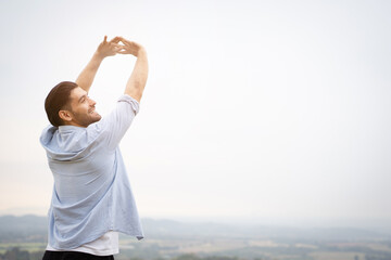 Happy handsome Middle - East Asian man standing on the mountain and making a relaxation with a beautiful landscape view. Man climb up on the top of mountain and posing for photography.