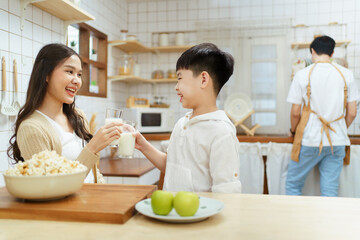 Asian cute little boy having a breakfast with his parent in a kitchen, boy holding a glass of milk and drink.