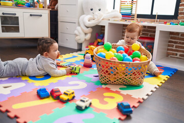 Two adorable babies playing with balls sitting on floor at kindergarten