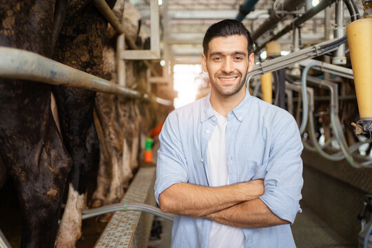 Happy cheerful Middle East - Asian male farmer making arms crossed and smiling to camera while standing in cow dairy farm. Male vet or veterinarian inspecting a livestock cows in farm.