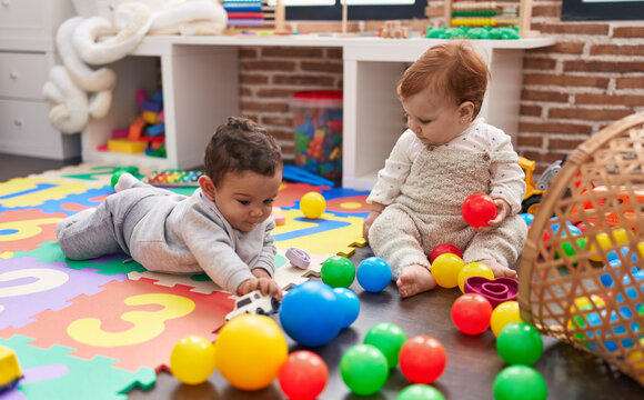 Two Adorable Babies Playing With Balls Sitting On Floor At Kindergarten