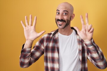 Hispanic man with beard standing over yellow background showing and pointing up with fingers number eight while smiling confident and happy.