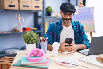 Young hispanic man artist using laptop and smartphone at art studio