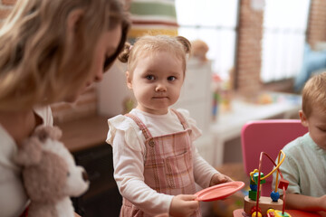 Teacher with boy and girl playing with toys sitting on table at kindergarten