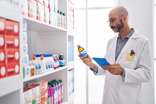 Young hispanic man pharmacist using touchpad holding medication bottle at pharmacy