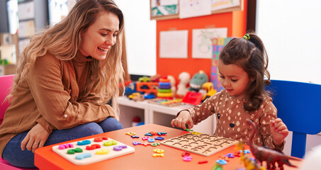 Fototapeta premium Teacher and toddler playing with maths puzzle game sitting on table at kindergarten