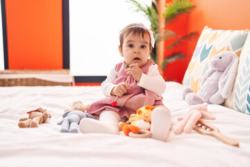 Adorable hispanic baby playing maraca sitting on bed at bedroom