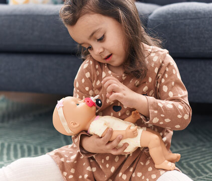 Adorable hispanic girl hugging baby doll sitting on floor at home